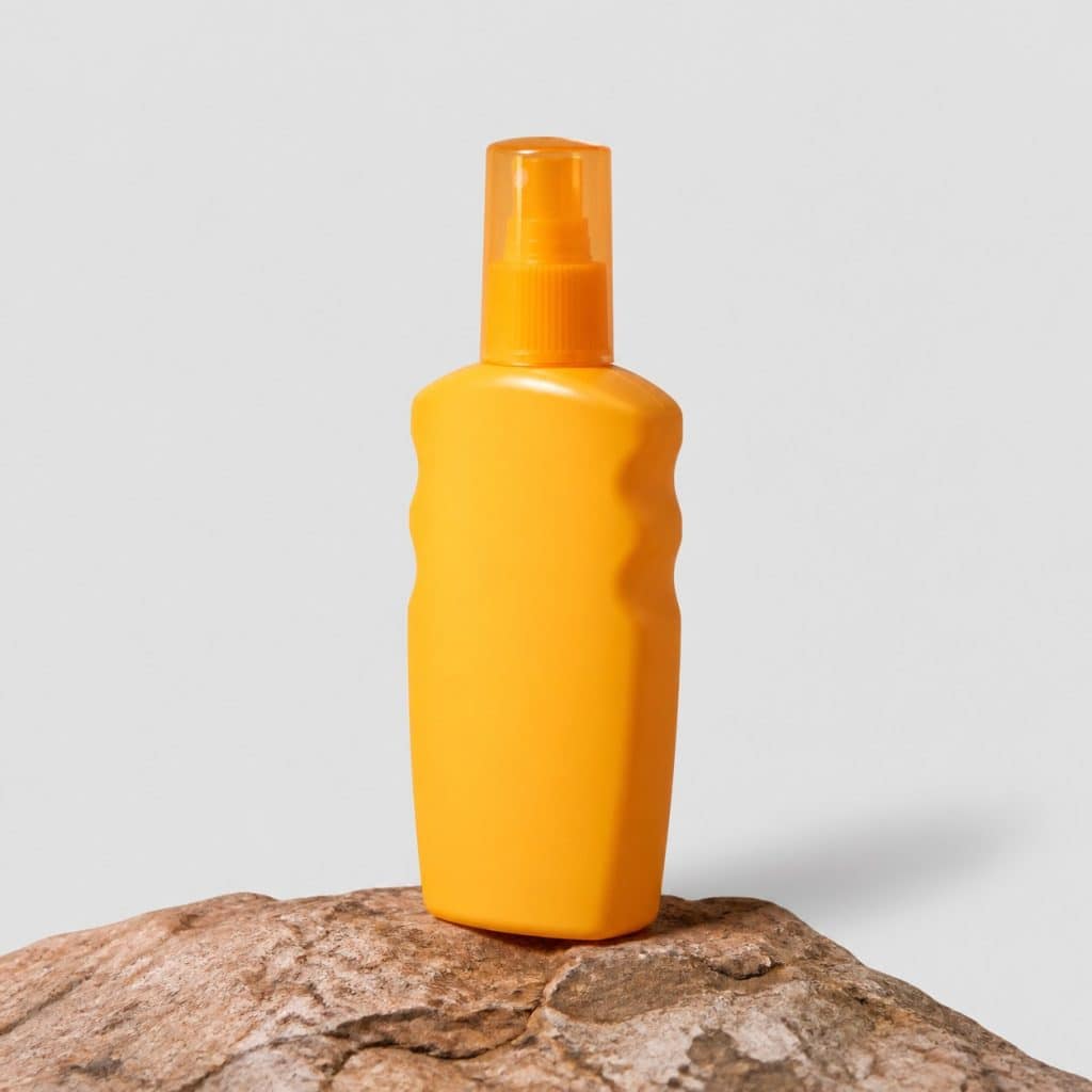 Flacon de spray solaire SPF50 posé sur un rocher en montagne